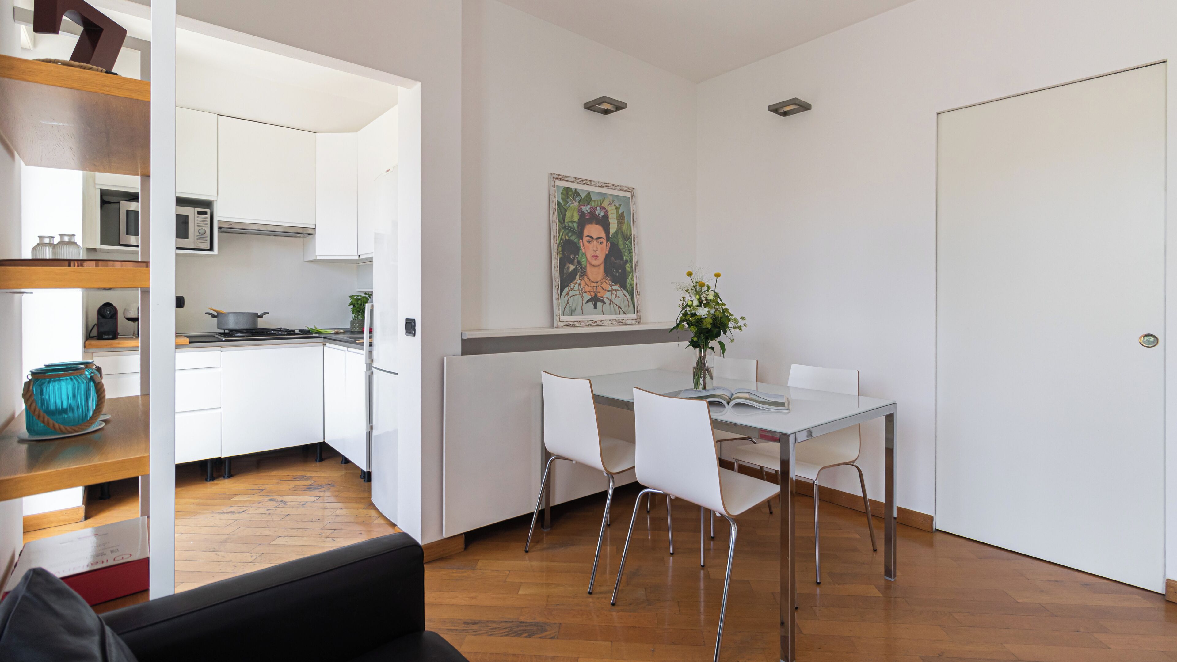 A modern kitchen with white cabinets, a dining table with chairs, and a painting on the wall.
