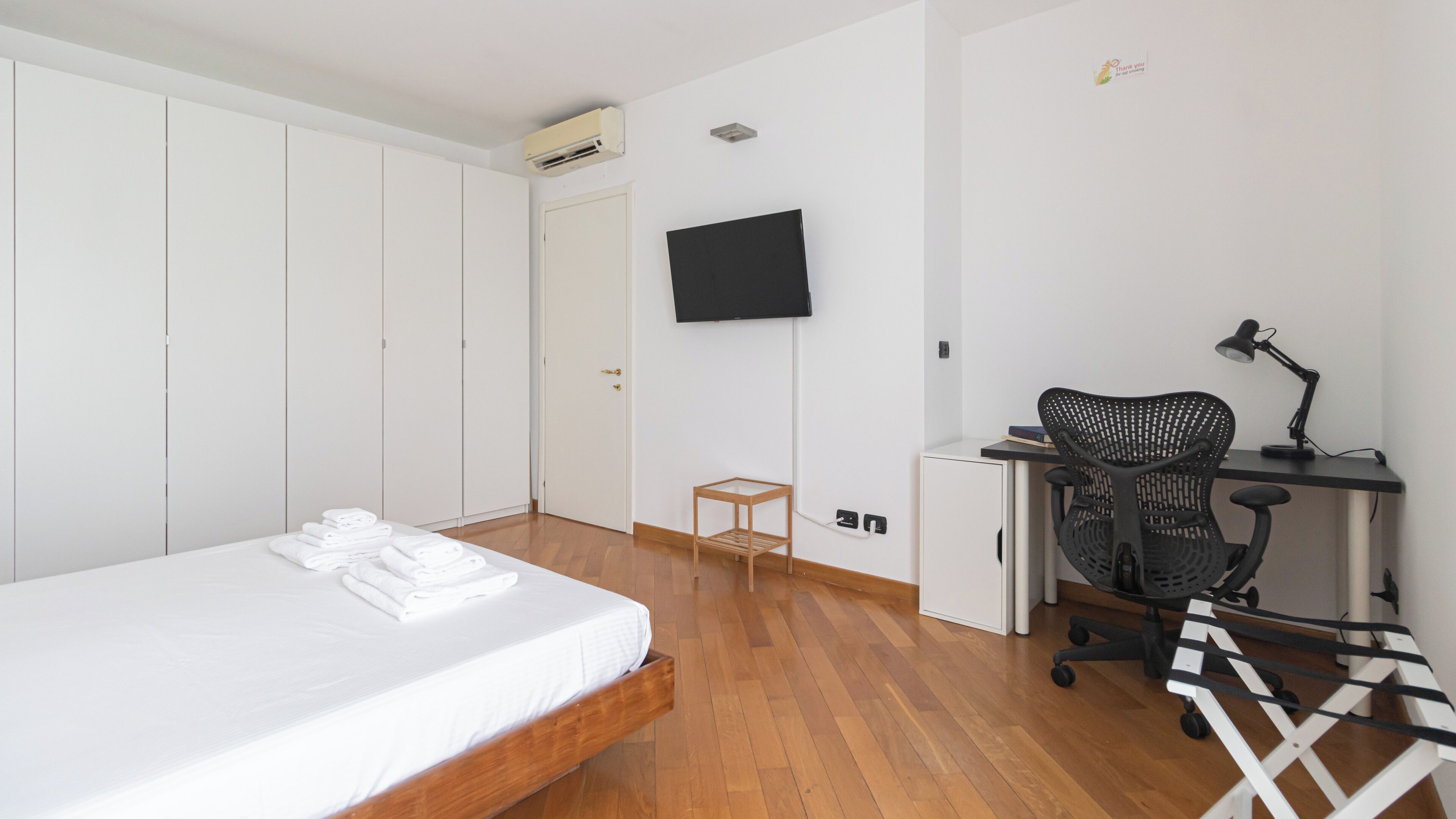 A bedroom with a bed, a desk with a chair, a TV, and a wardrobe.