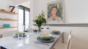 Un comedor moderno con una larga mesa dispuesta para cuatro personas, con vasos, platos y tazones transparentes. Un cuadro grande enmarco la pared sobre la mesa.
