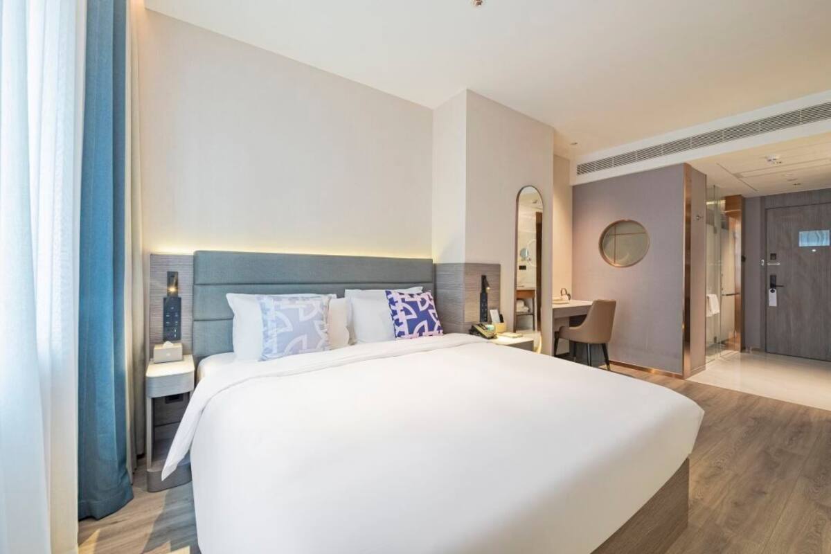 Una habitación de hotel moderna con una cama grande, mesitas de noche, un escritorio y un espejo.