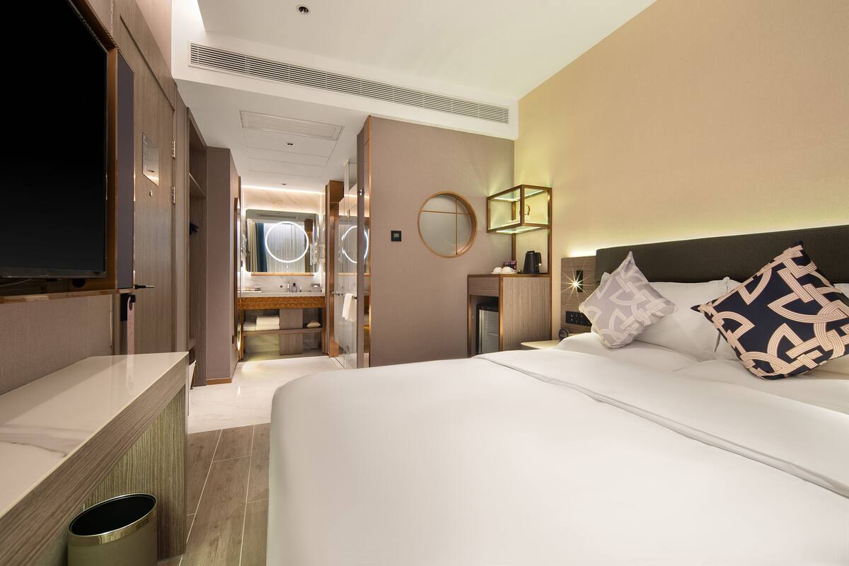 Una habitación de hotel con una cama grande, un televisor, un baño con espejo y una mesita.