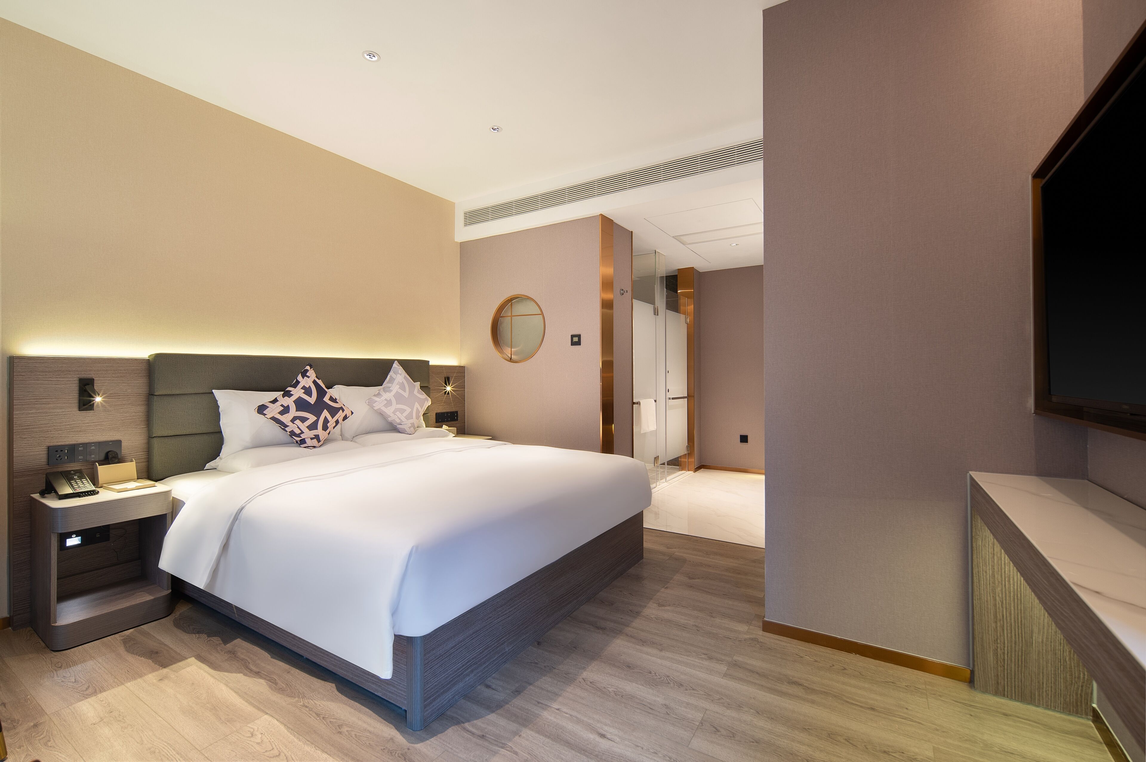A modern hotel room with a large bed, a bedside table with a lamp, a TV mounted on the wall, and a walk-in closet.