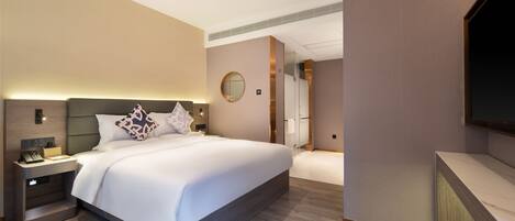 A modern hotel room with a large bed, a bedside table with a lamp, a TV mounted on the wall, and a walk-in closet.