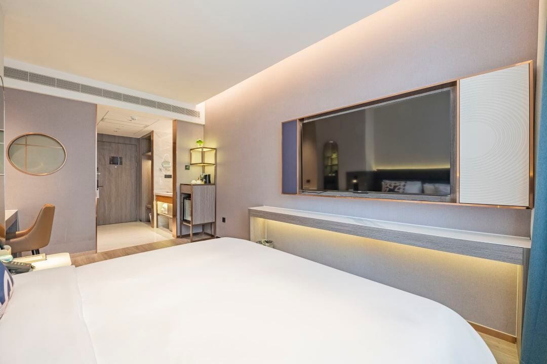 A modern hotel room with a large bed, a desk, a chair, a mirror, and a TV.