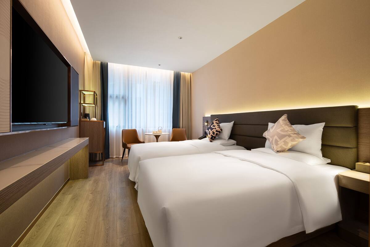 Una habitación de hotel con dos camas, televisión, escritorio y ventana con cortinas.