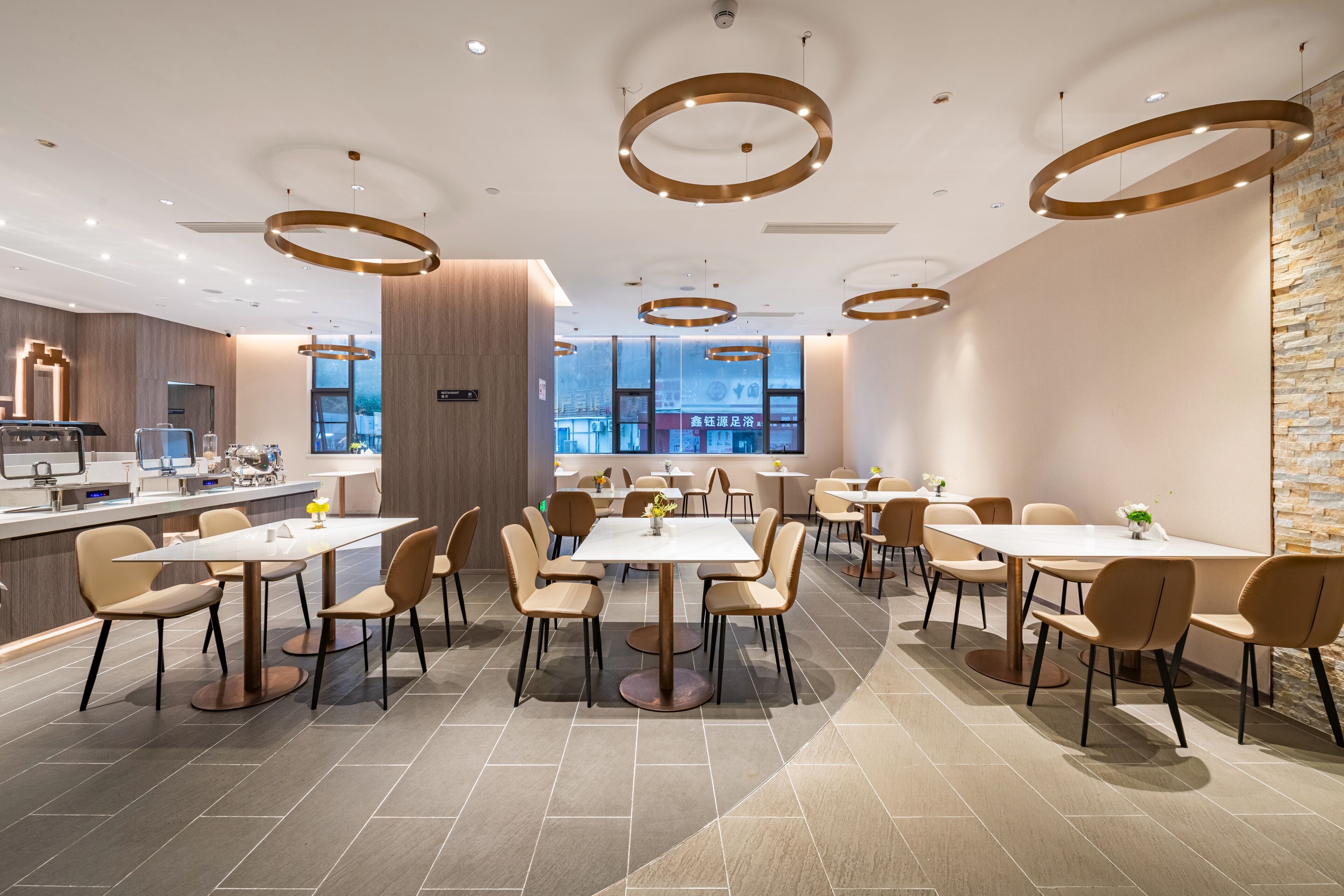 Un restaurante moderno con mesas y sillas redondas, una zona de bar y amplios ventanales con vista a la ciudad.