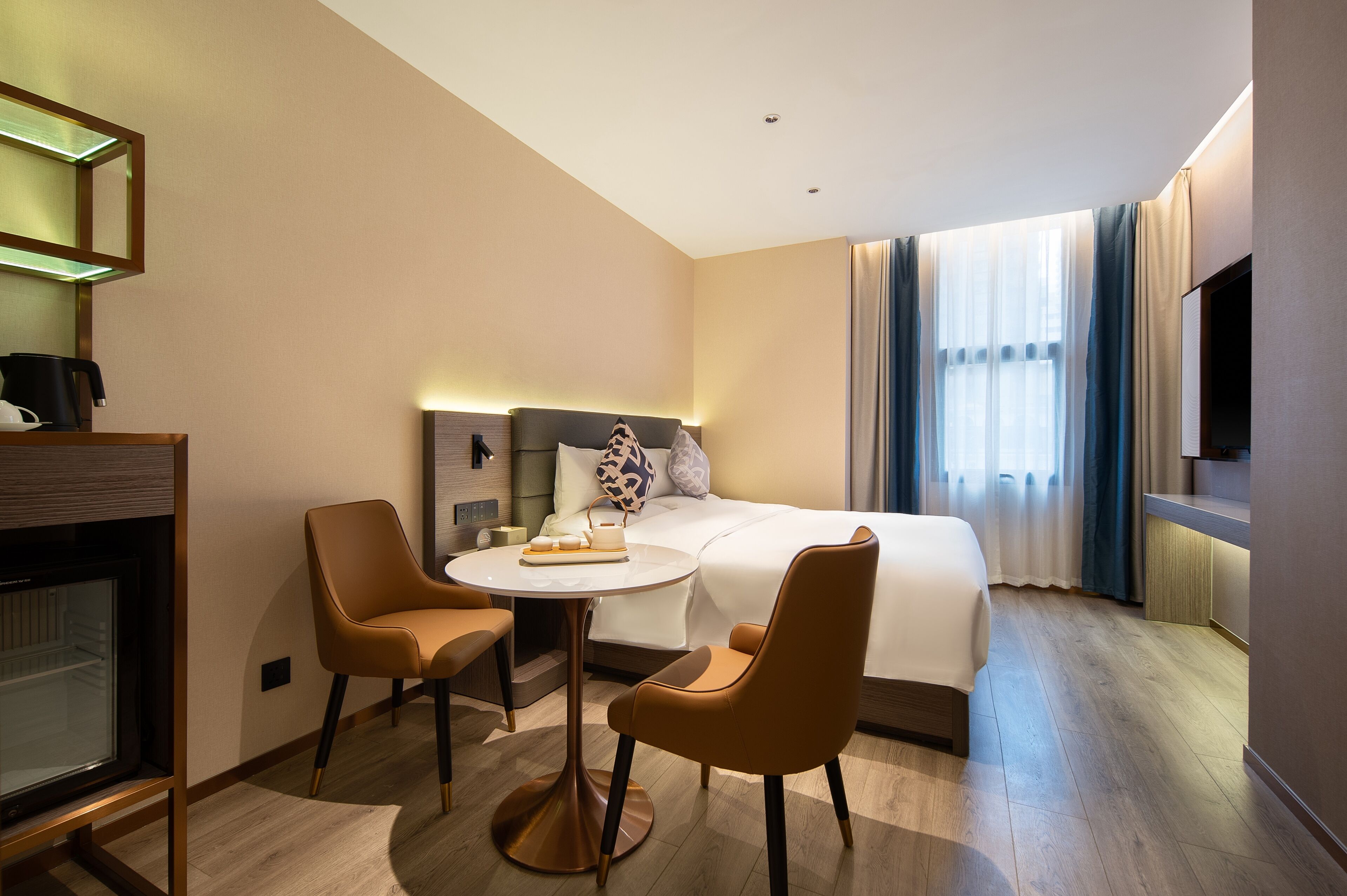 Une chambre d’hôtel comprenant un lit, une table ronde avec des chaises, un téléviseur et un minibar.