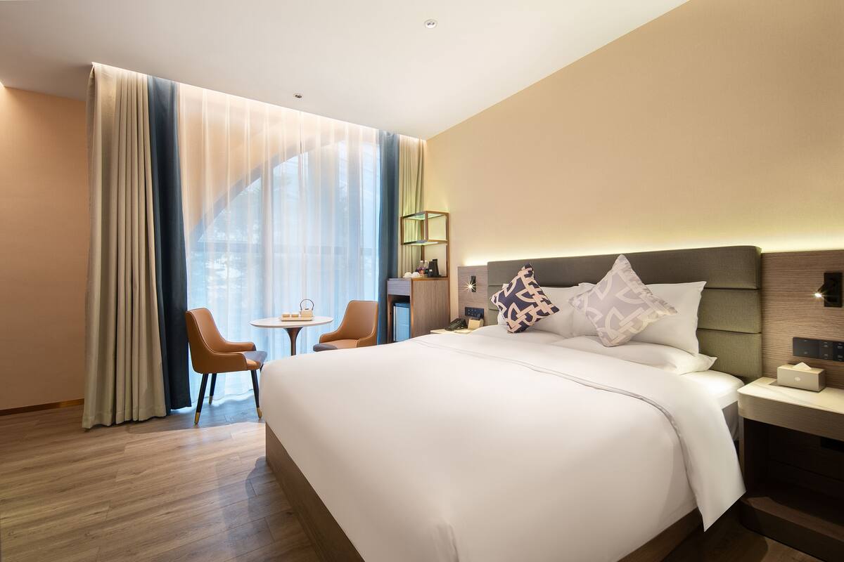Habitación de hotel con una cama grande, un escritorio con silla y un ventanal con cortinas.