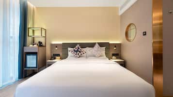 A modern hotel room with a large bed, bedside tables, a TV, and a mirror on the wall.