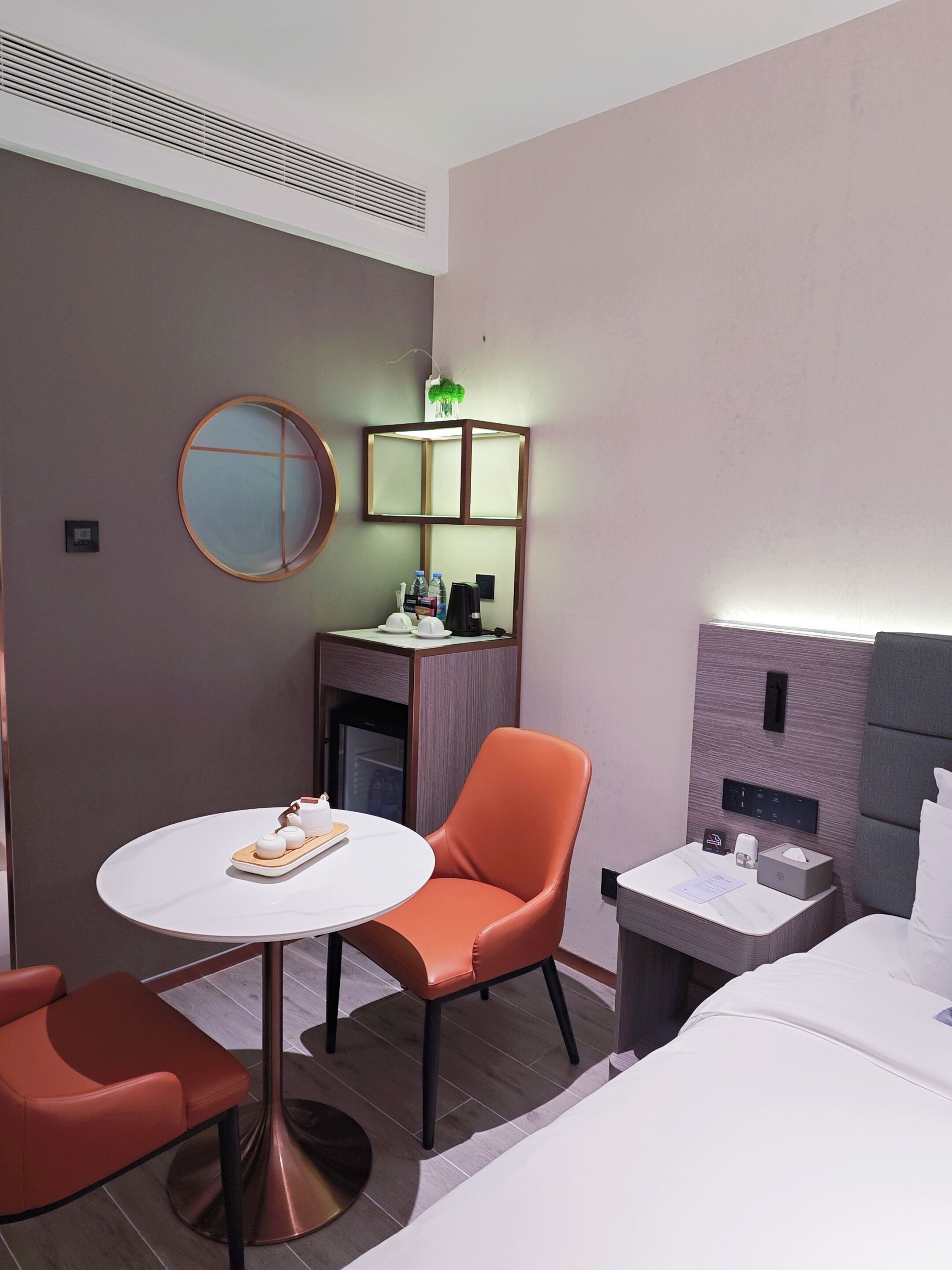 A modern hotel room with a round table, orange chair, and a bed with white linens.