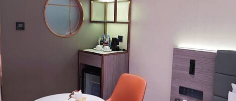 A modern hotel room with a round table, orange chair, and a bed with white linens.