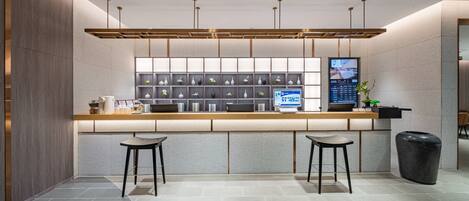 A modern reception area with a counter, two stools, a digital screen, and a plant.