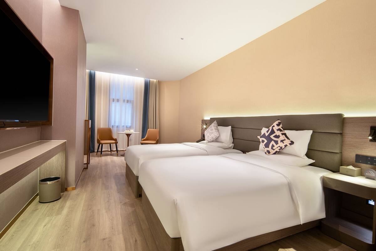 Habitación de hotel con dos camas, televisión, una mesita y una silla.