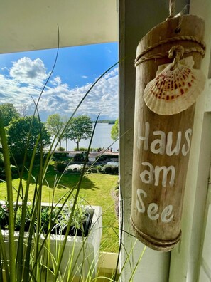 Vista desde un balcón con un letrero de madera que dice 'Haus am See' y un lago al fondo.