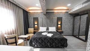 Una habitación de hotel moderna con una cama grande, un escritorio, una silla y un amplio ventanal con cortinas.