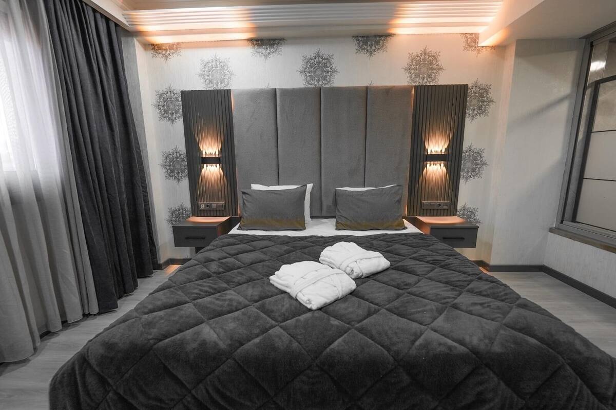A modern hotel room with a large bed, two bedside tables with lamps, and a decorative wall panel.