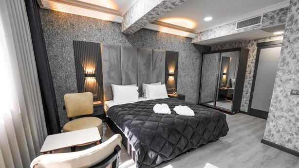 Una habitación de hotel moderna con una cama grande, dos mesitas de noche, una silla y un espejo.