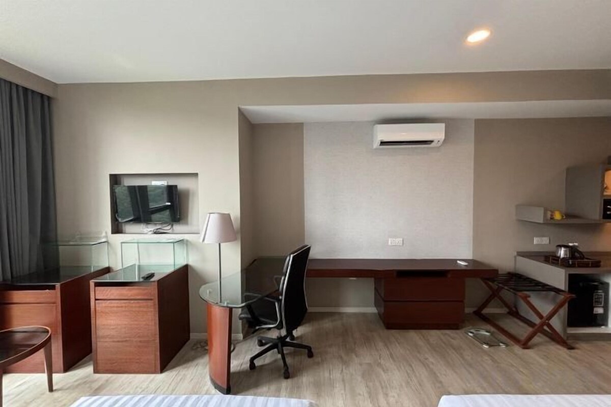 Una habitación de hotel con escritorio, una silla, televisión y kitchenette.