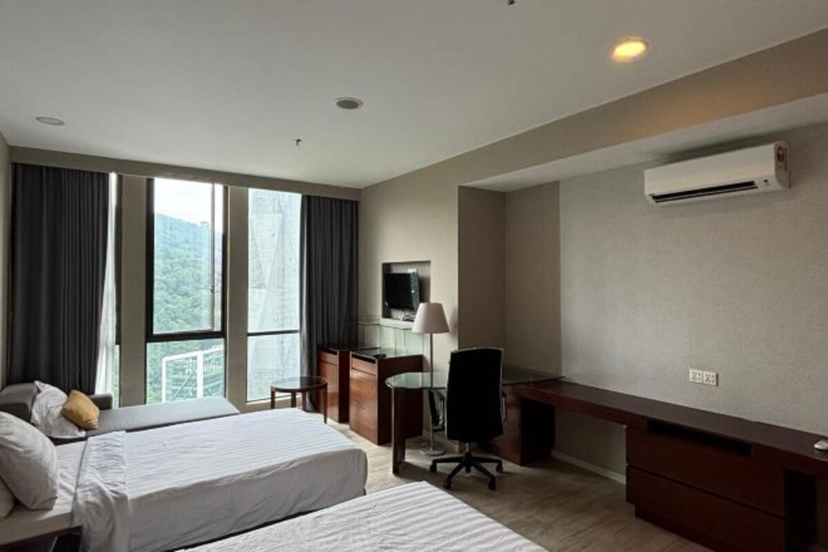 A hotel room with two beds, a desk, a chair, a TV, and an air conditioning unit.