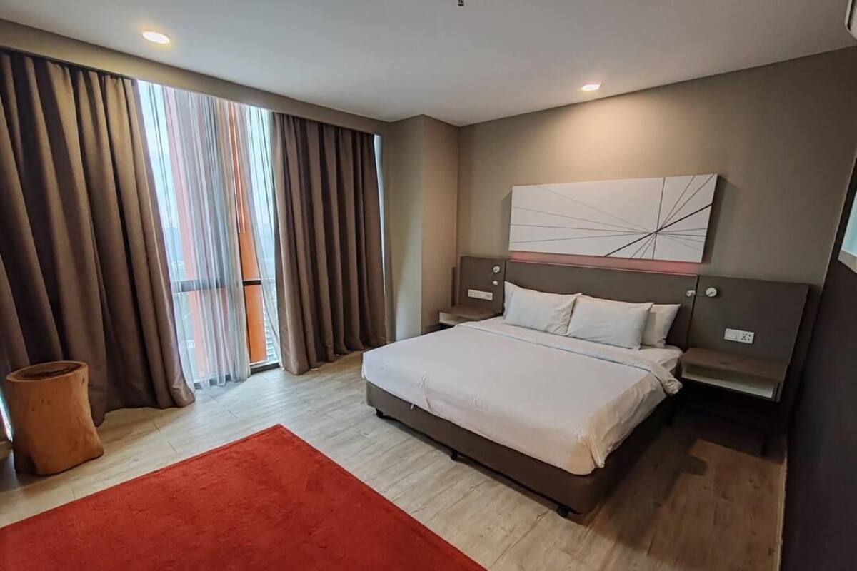 A modern hotel room with a large bed, a red rug, and a view through the curtains.
