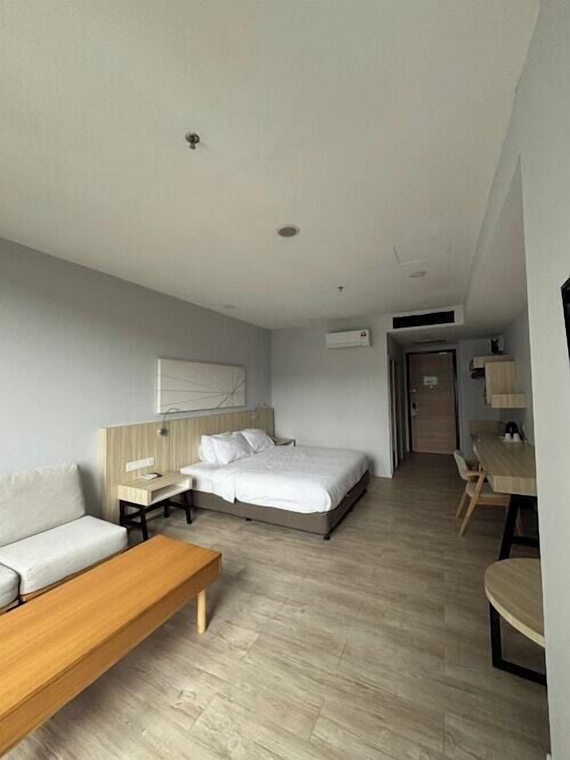 A modern hotel room with a bed, a sofa, a wooden bench, and a desk.