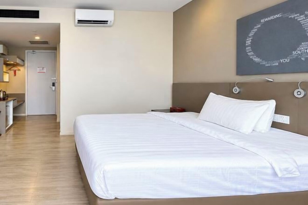 A hotel room with a bed, bedside table, and a wall-mounted air conditioner.