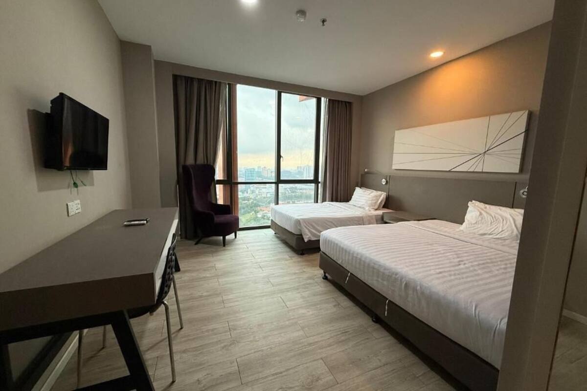 A hotel room with two beds, a desk, a chair, a TV, and a large window with curtains.