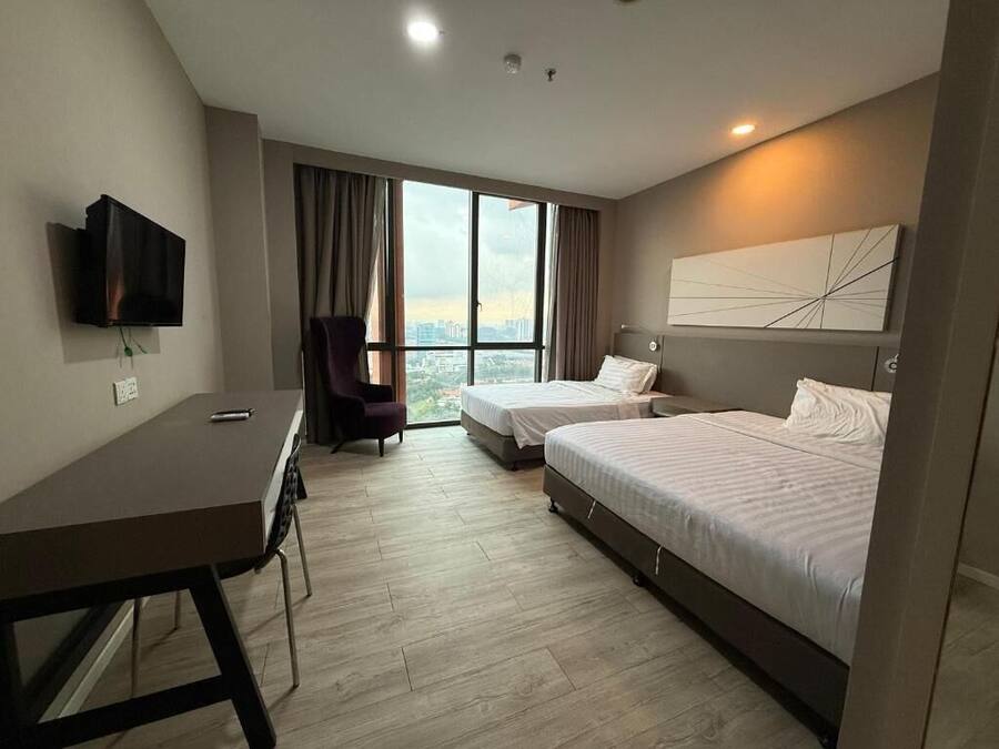 Hotelkamer met twee bedden, een bureau, een stoel, een televisie en een groot raam met gordijnen.