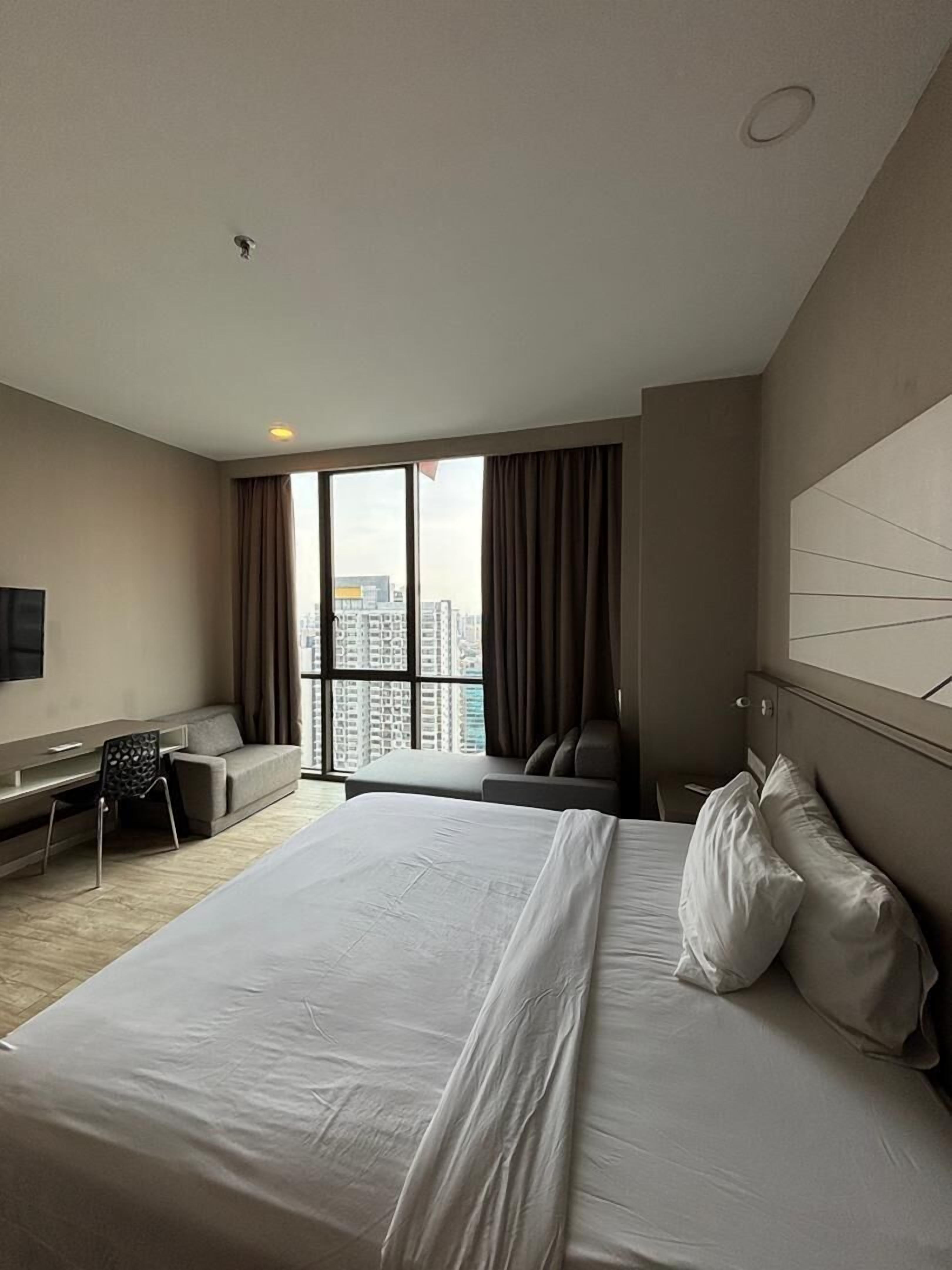Une chambre d’hôtel moderne, dotée d’un grand lit, d’un bureau et offrant une vue sur le paysage urbain.