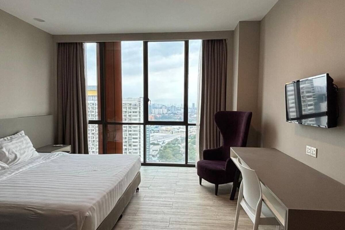 A hotel room with a bed, a desk, a chair, a TV, and a large window with curtains.