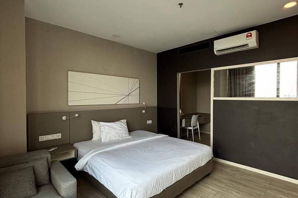 A modern hotel room with a large bed, a sofa, a desk, and an air conditioning unit.