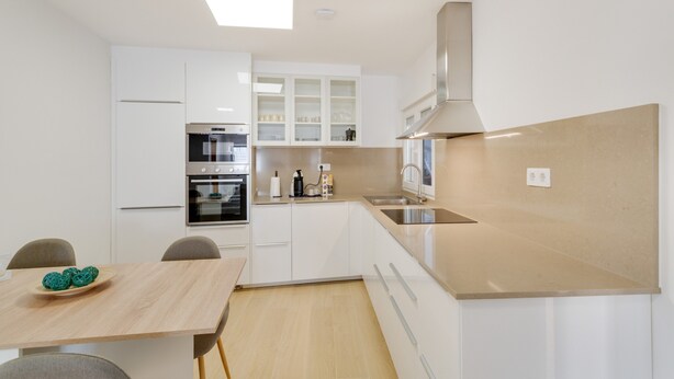 A modern kitchen with white cabinetry, a built-in oven, and a stainless steel range hood.