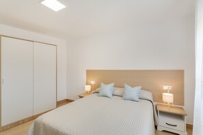 A bedroom with a bed, two bedside tables, a nightstand, a wardrobe, and a ceiling light.