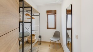 A room with a bunk bed, a chair, a small table with a basket, a window, and a mirror.