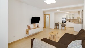 A modern living room with a flat-screen TV, a sofa, a coffee table, and a kitchen in the background.