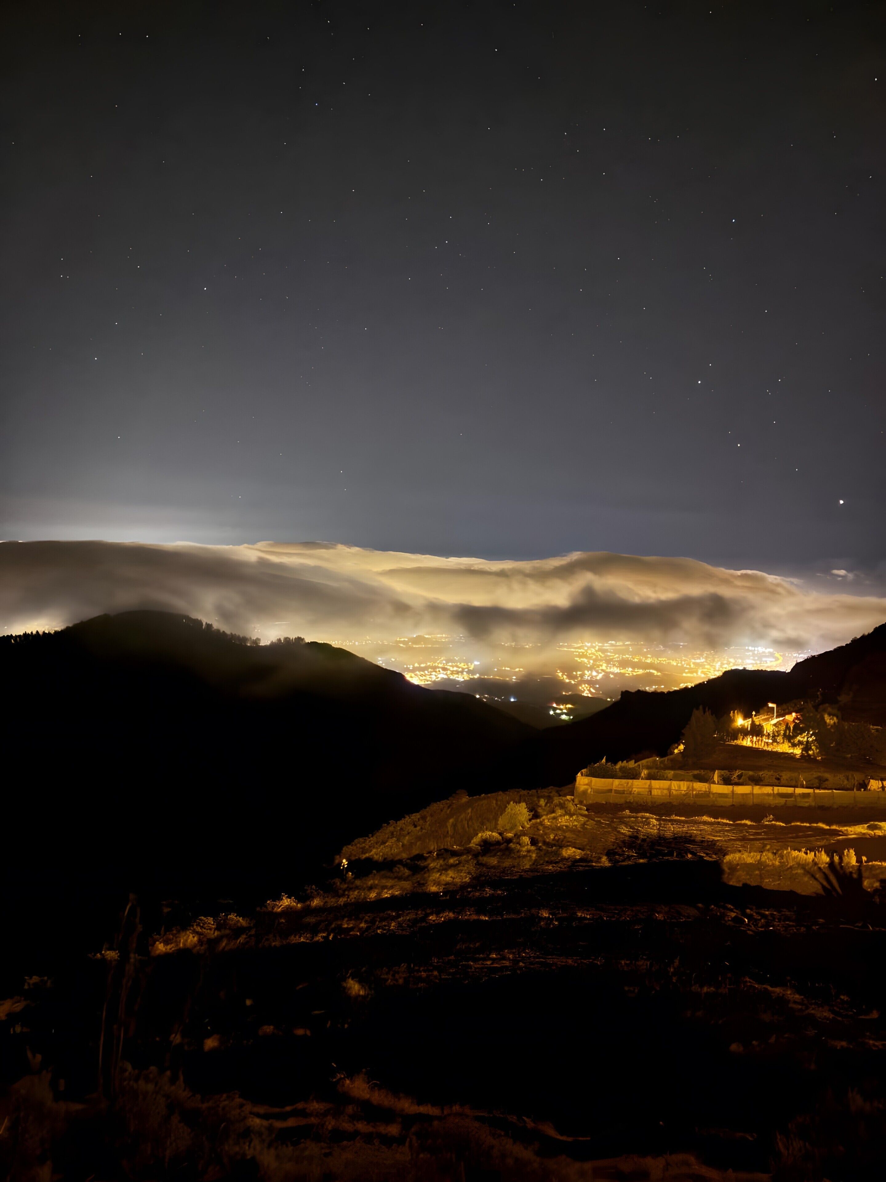 Un paysage nocturne avec une ville située dans la vallée, des bâtiments illuminés et un ciel étoilé.