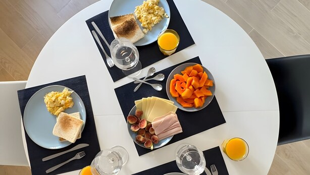 Una tavola imbandita con uova strapazzate, pane tostato e frutta, accompagnata da posate e bicchieri.