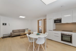 A modern kitchen with white cabinets, a built-in oven, and a dining area with a round table and chairs.