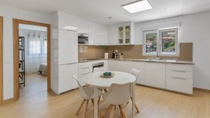 Una cucina moderna con mobili bianchi, un tavolo da pranzo con sedie e vista sull'esterno attraverso una finestra.