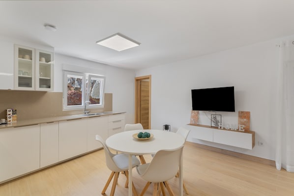 A modern kitchen with white cabinetry, a dining table with chairs, a built-in TV, and a window with a view.
