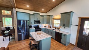 A modern kitchen with light blue cabinets, stainless steel appliances, and a central island with stools. - Luxe Cabin, View, 4 Bedrooms, Hot Tub, 3 Kings, Private, 8 min to DT BR (Blue Ridge)