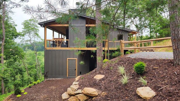 A modern cabin with a wooden deck, a stone foundation, and a view of the surrounding forest. - Luxe Cabin, View, 4 Bedrooms, Hot Tub, 3 Kings, Private, 8 min to DT BR (Blue Ridge)