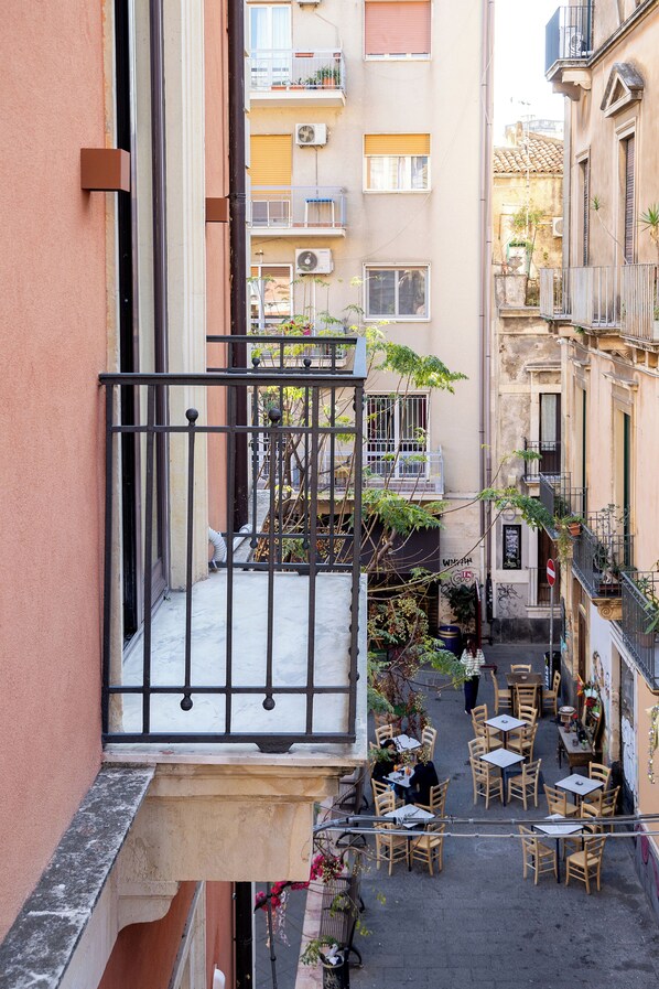 A narrow alley with a small outdoor seating area with tables and chairs, surrounded by buildings with balconies and windows.
