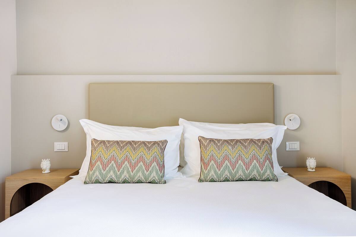 A neatly made bed with white linens, two pillows with a zigzag pattern, and a wooden headboard.