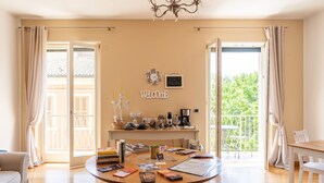 A cozy living room with a round coffee table, a sofa, and a dining area. A balcony with a view of greenery is visible through the open door. - Charming abode with Arena view | 3 cam. 6 guests (Verona)