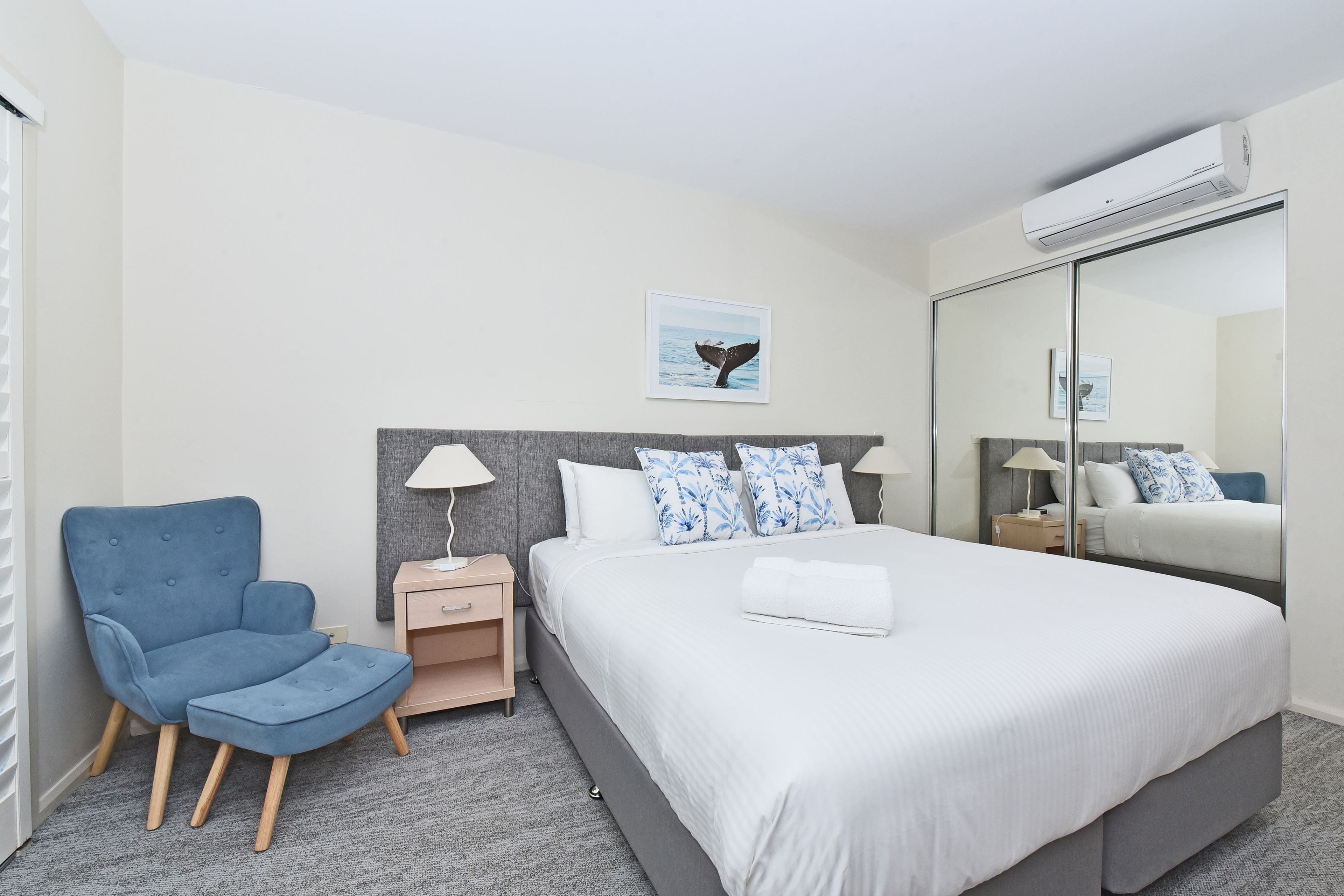 A hotel room with a bed, a chair, a nightstand, a lamp, and a wall-mounted air conditioner.