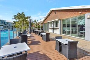 Een terras buiten met tafels en stoelen, een zwembad en een gebouw met grote ramen.
