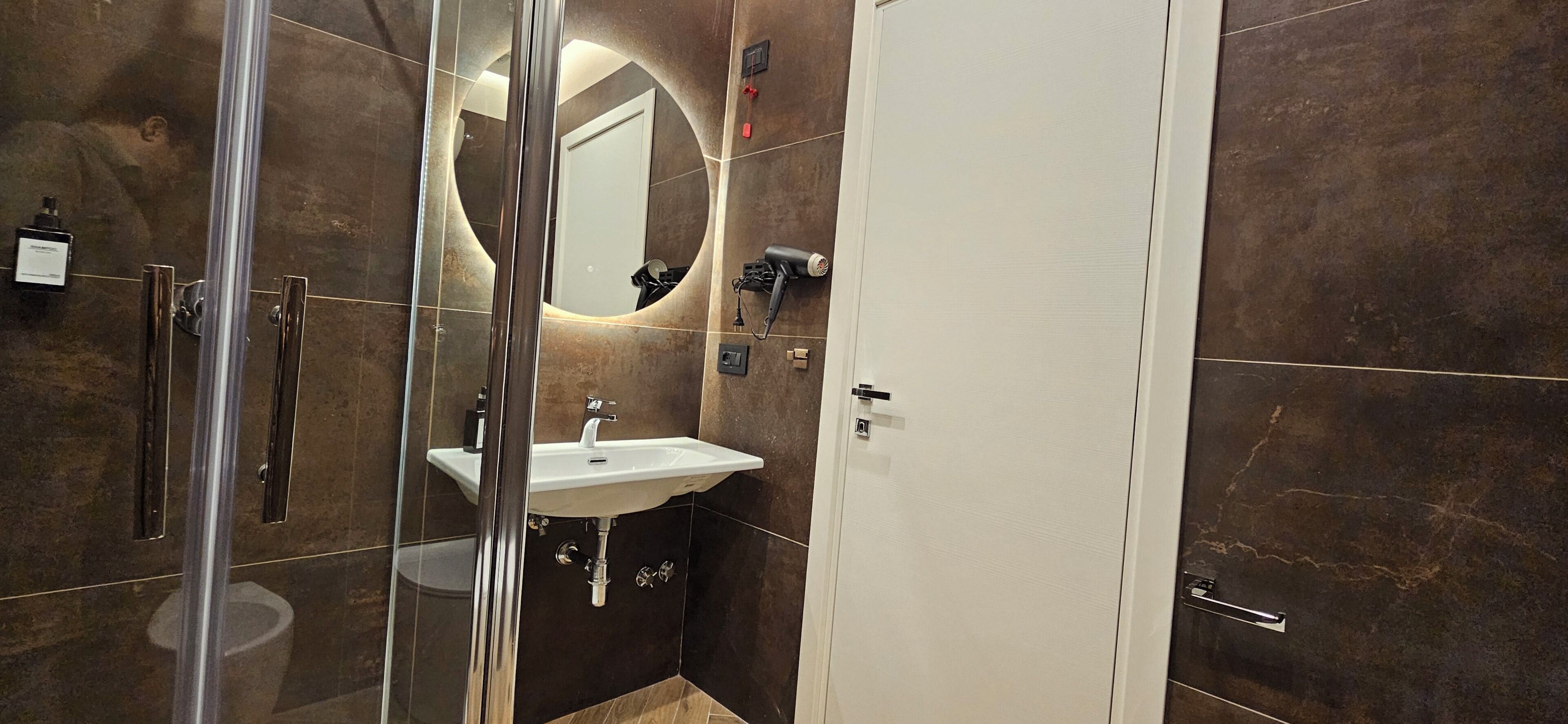 A modern bathroom with a glass shower enclosure, a white sink, and a large mirror.
