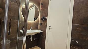 A modern bathroom with a glass shower enclosure, a white sink, and a large mirror.