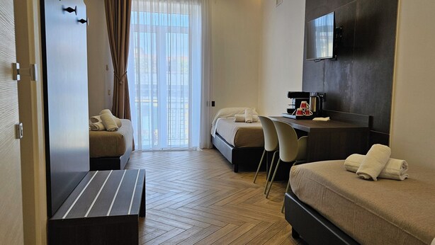Una habitació d'hotel amb un llit, una escriptori amb una cafetera, una cadira i un televisor fixat a la paret.